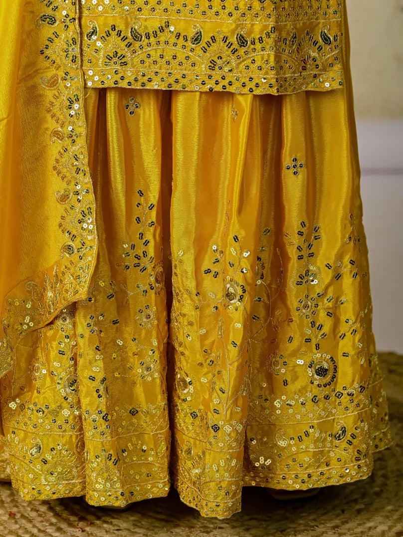 Yellow traditional outfit with intricate black embroidery on a neutral background