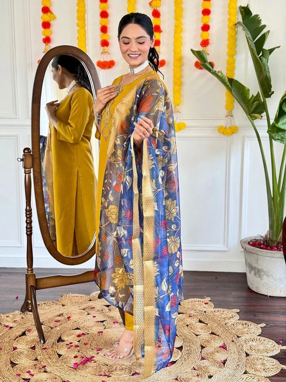Woman in a blue floral saree with gold border standing next to a mirror, decorated room.