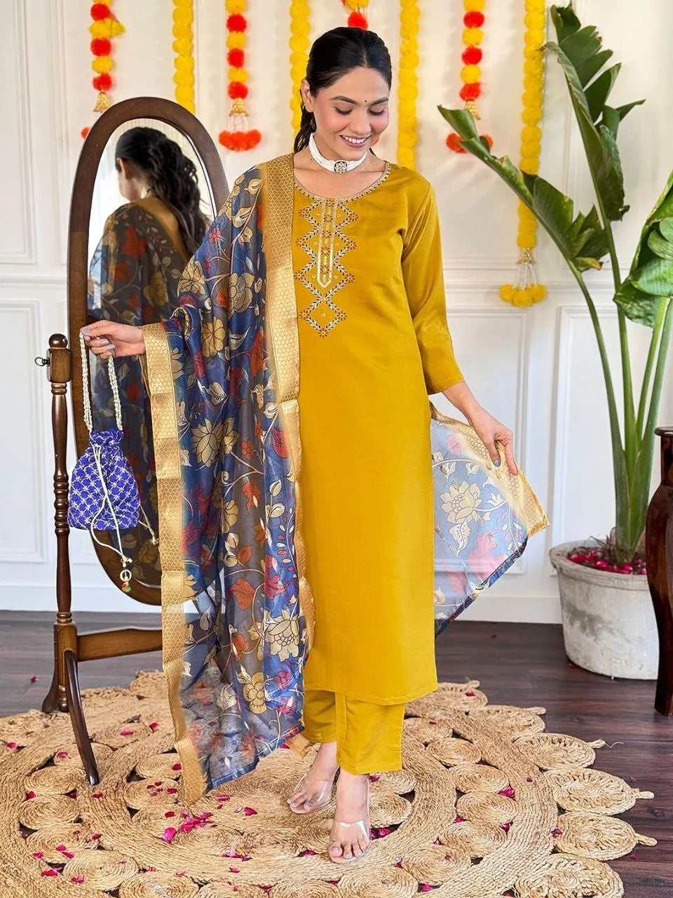 Woman in a yellow traditional outfit standing next to a mirror with decorative elements in the background.