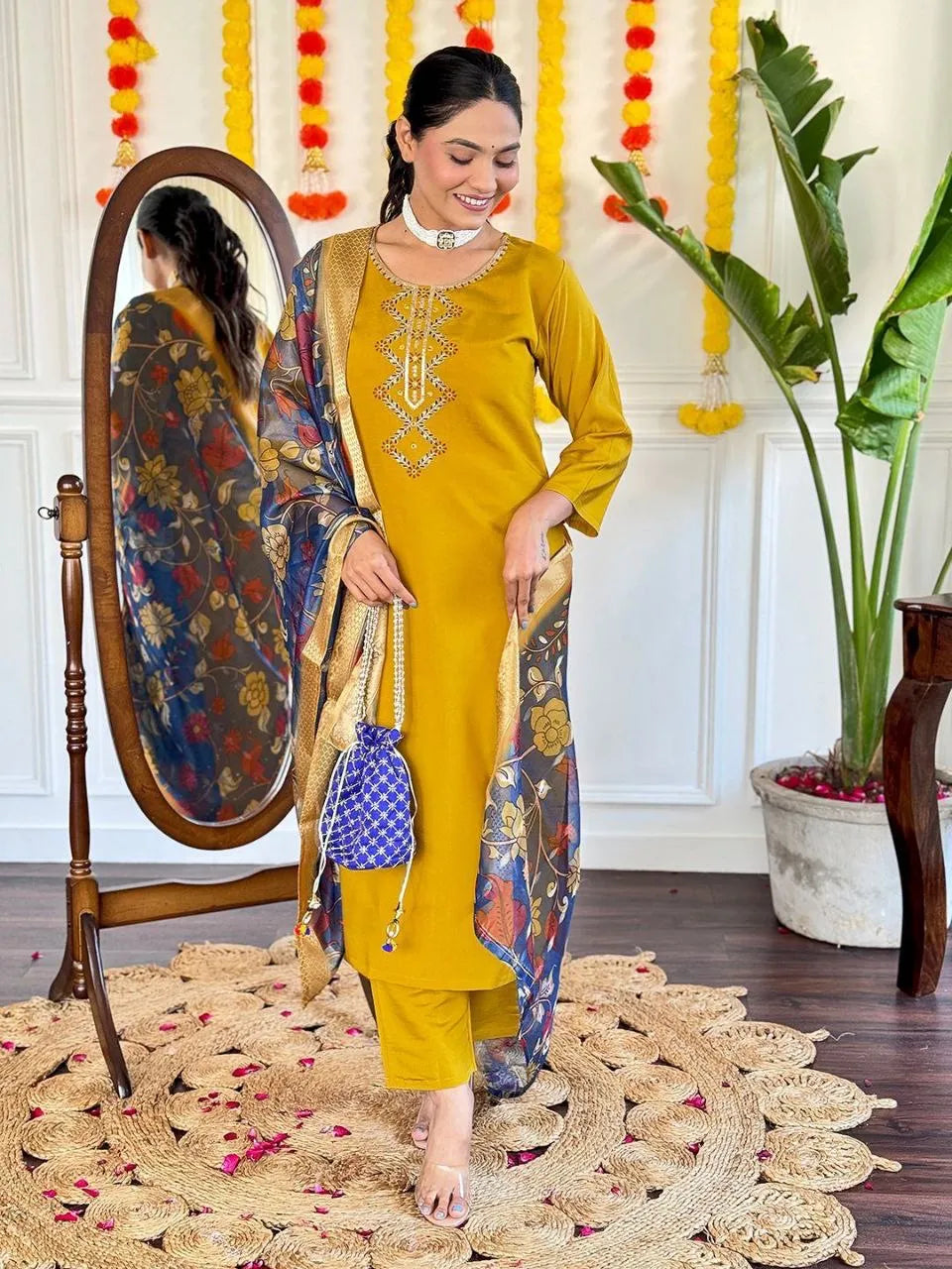 Woman in a yellow traditional outfit standing next to a mirror with decorative elements in the background.