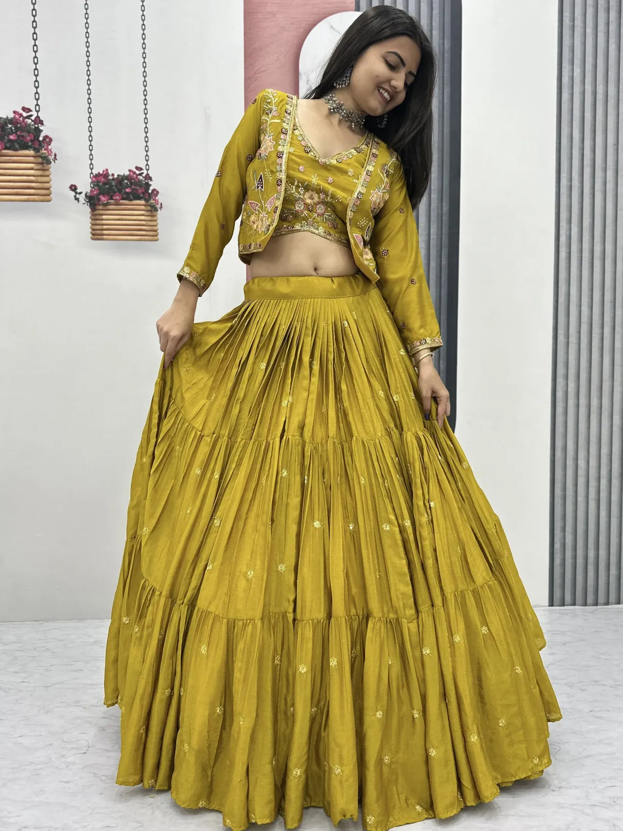 Woman wearing a mustard yellow traditional outfit with a matching skirt in a minimal indoor setting.