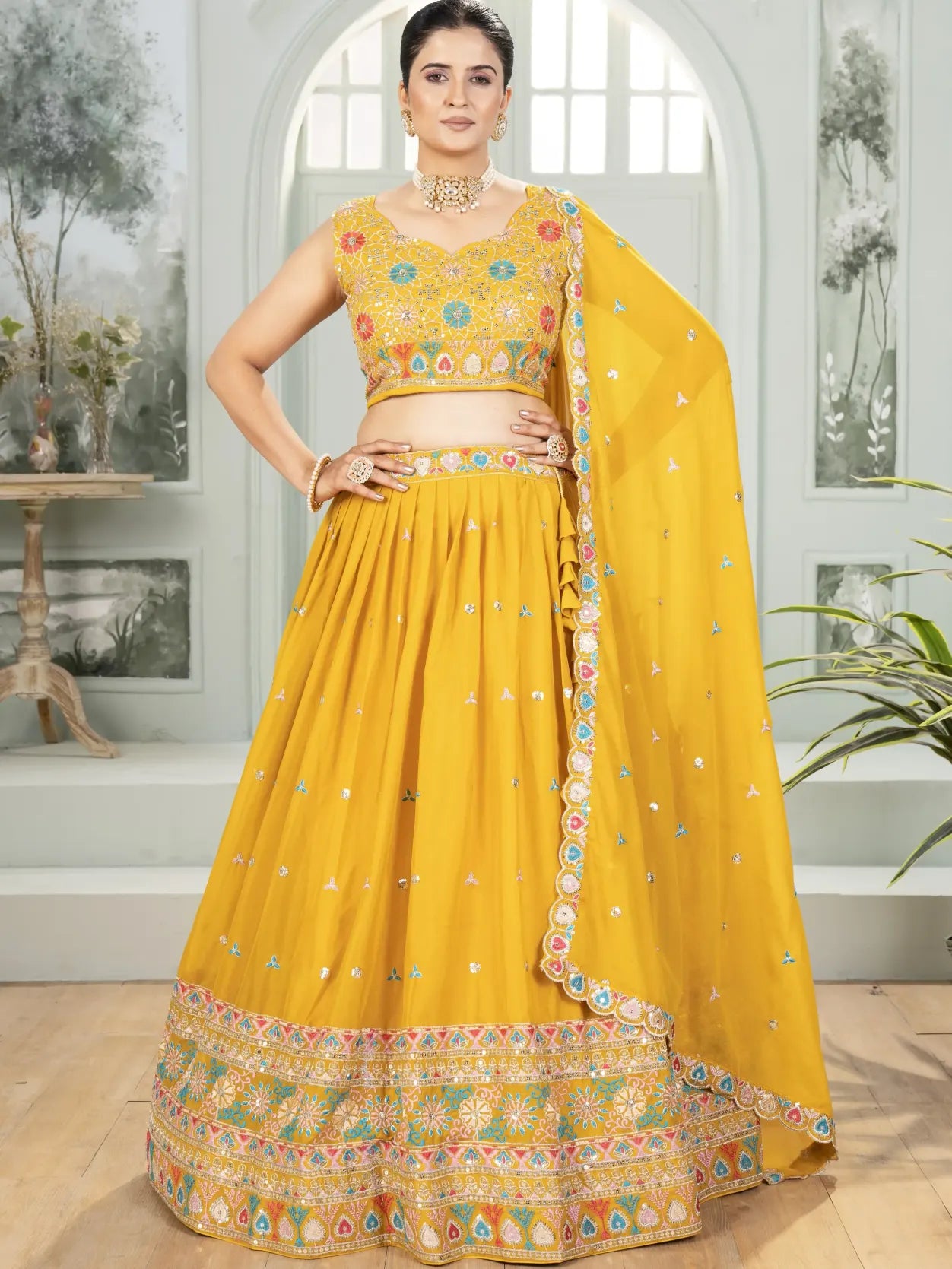 Woman wearing a yellow traditional outfit with floral patterns indoors.