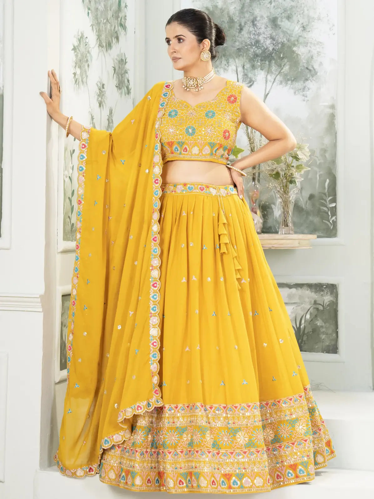 Woman wearing a yellow traditional outfit with floral patterns indoors.