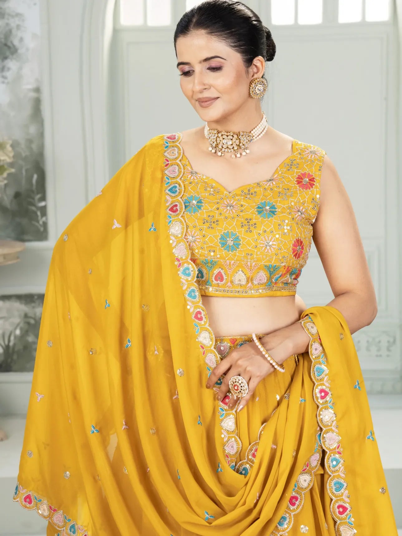 Woman wearing a yellow saree with intricate designs indoors.