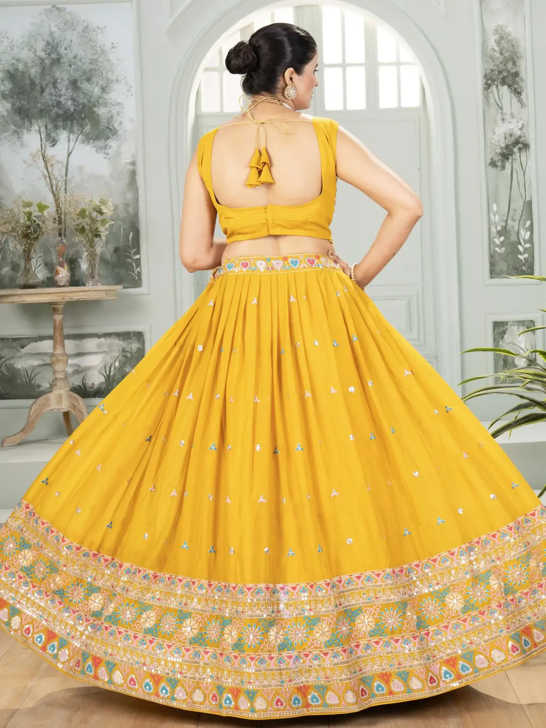 Woman wearing a yellow traditional outfit with a floral patterned skirt in an indoor setting.