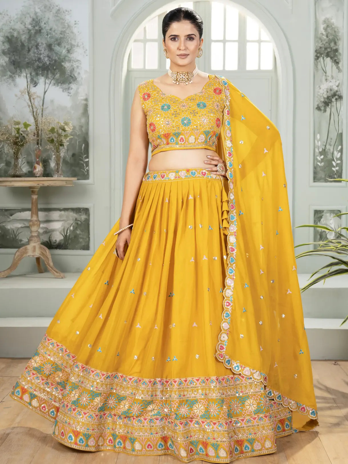 Woman wearing a yellow embroidered traditional outfit in a decorated room.
