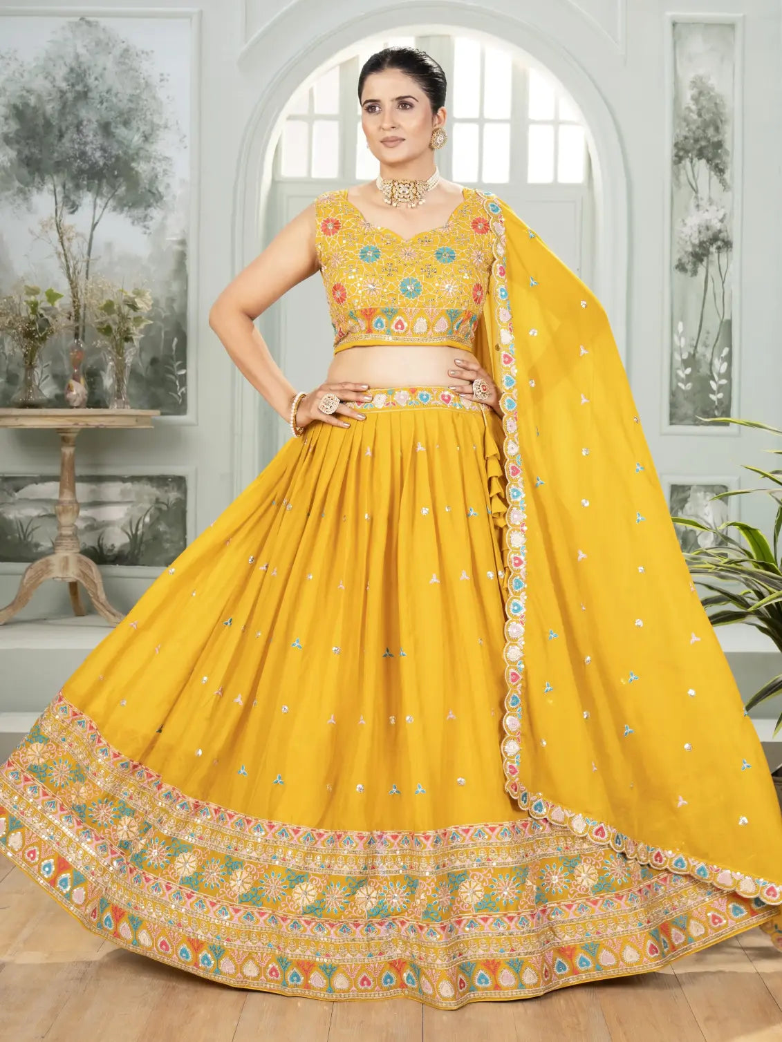 Woman wearing a yellow traditional outfit with floral patterns in a room setting.