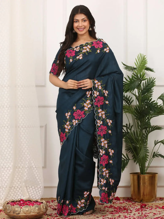 Woman wearing a dark blue saree with floral embroidery in a home setting.