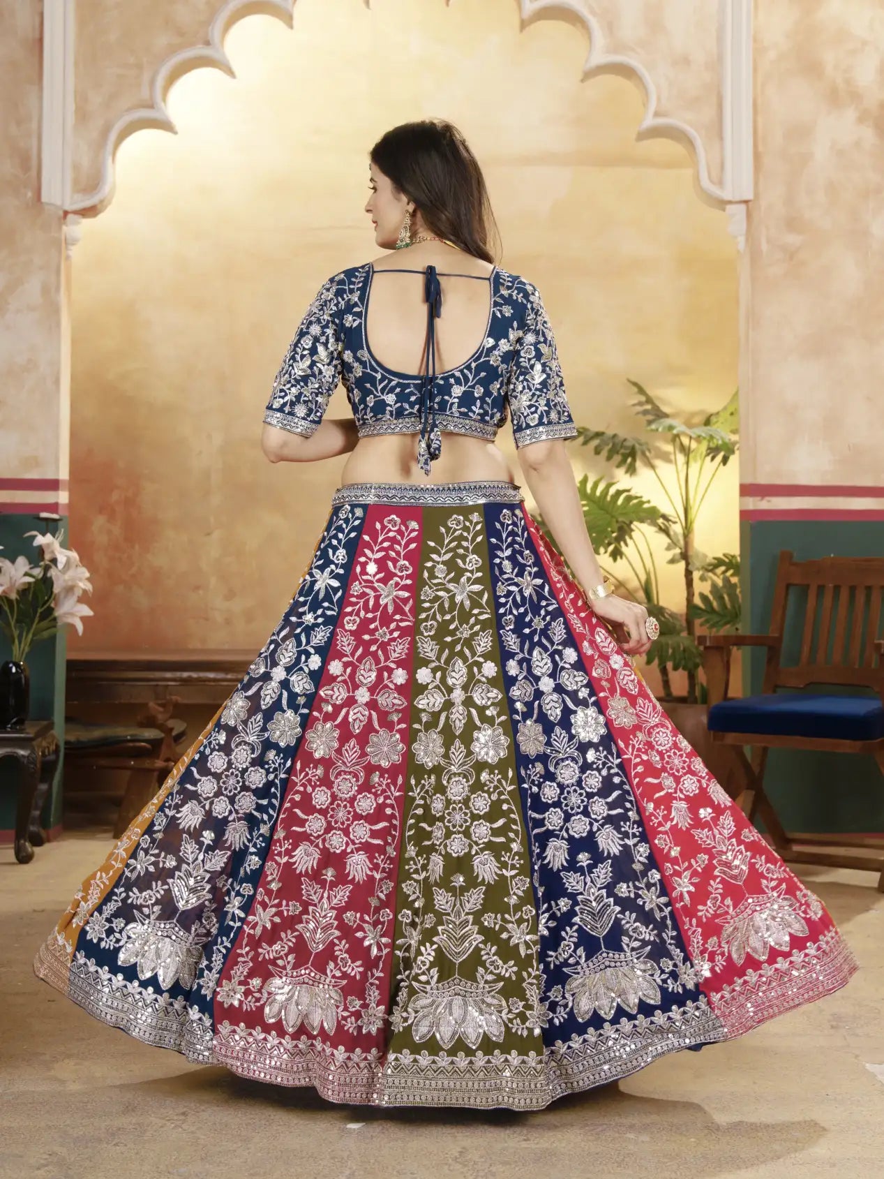 Woman wearing a colorful embroidered traditional outfit in a decorated room.