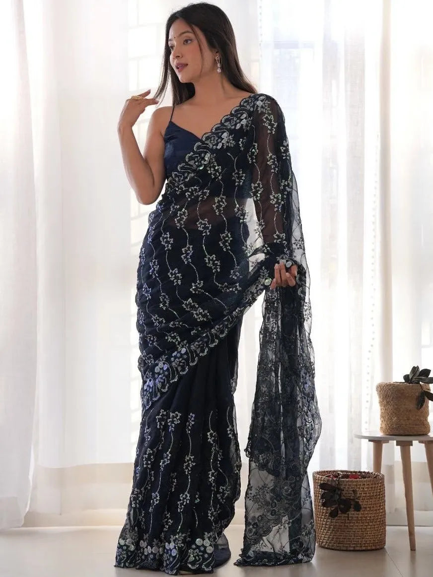 Woman wearing a dark blue saree with white floral patterns in a bright room.