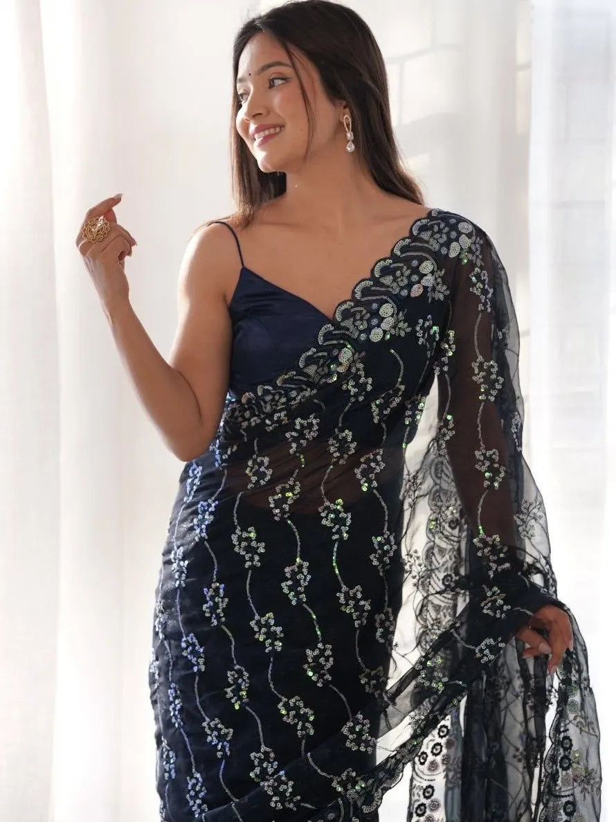 Woman wearing a navy blue saree with white patterns against a white curtain background