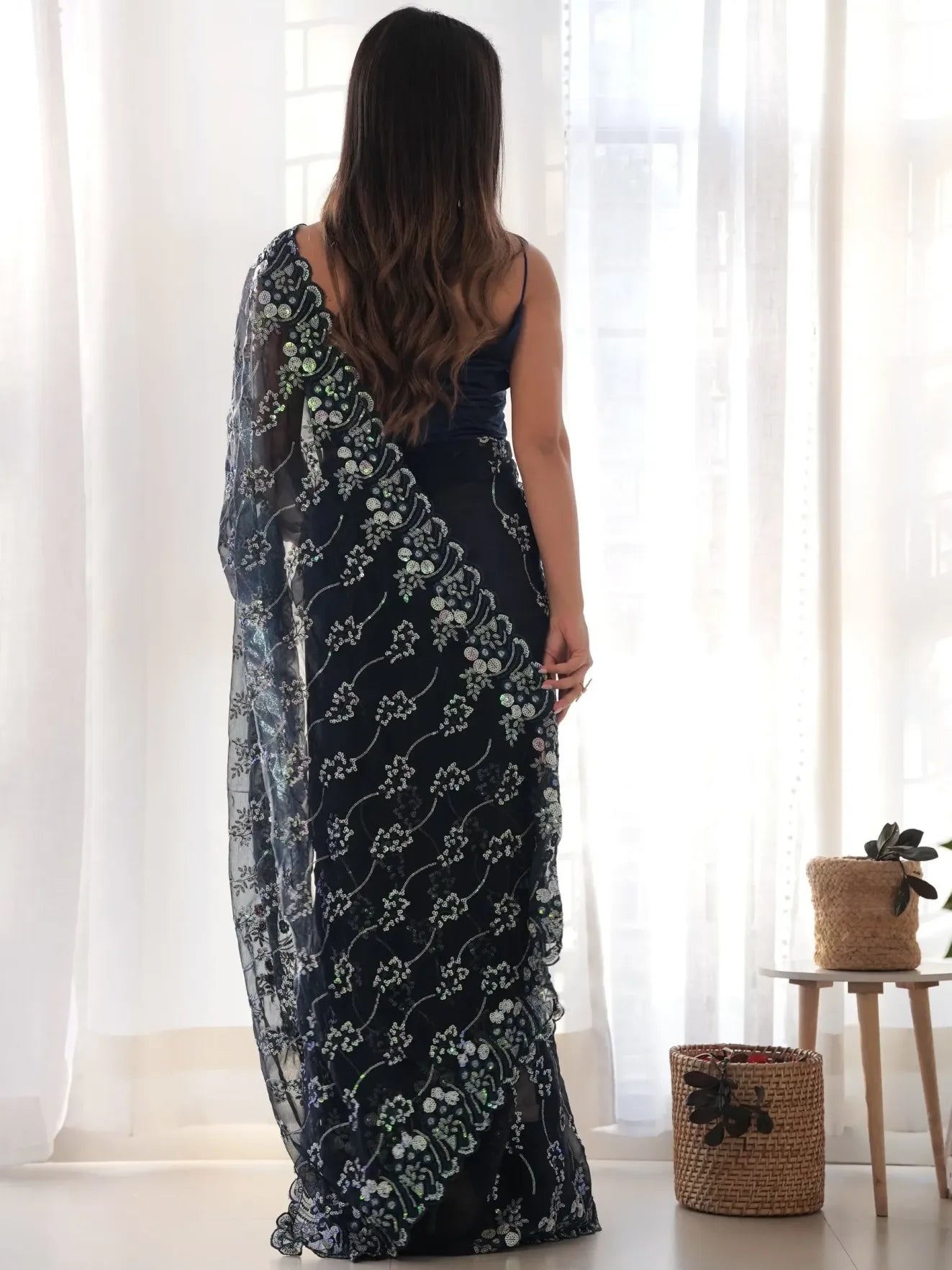 Woman wearing a long dark blue floral dress standing in a bright room with white curtains.