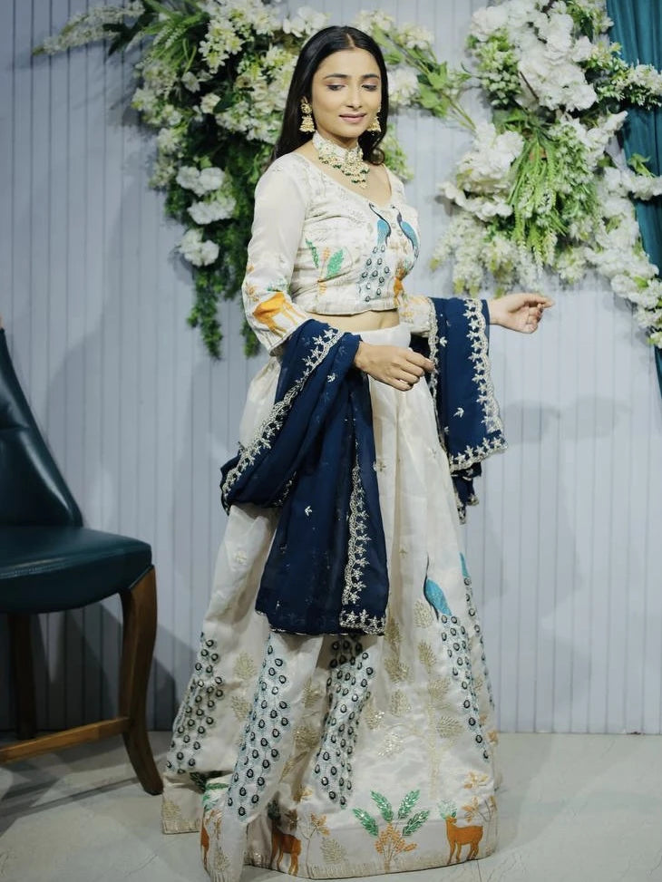 Woman in traditional outfit with floral and animal patterns, standing against a decorated background.