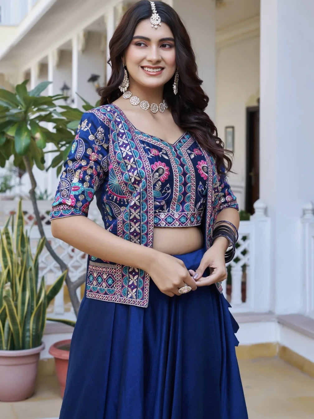 Woman wearing a traditional outfit with a colorful top and blue skirt in an outdoor setting.