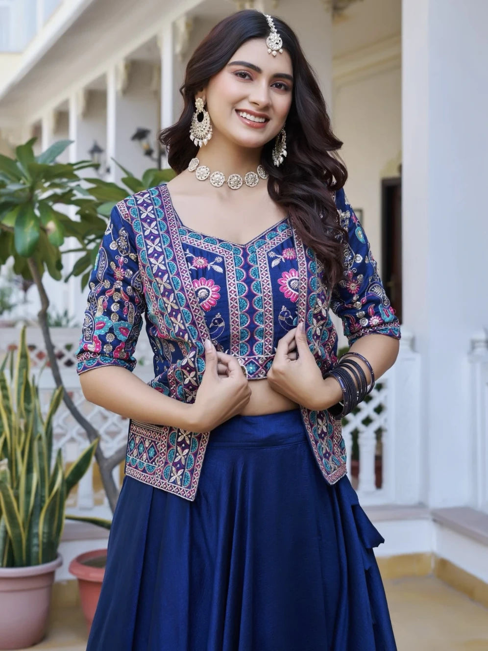 Woman in a traditional outfit with intricate patterns and jewelry, standing outdoors.