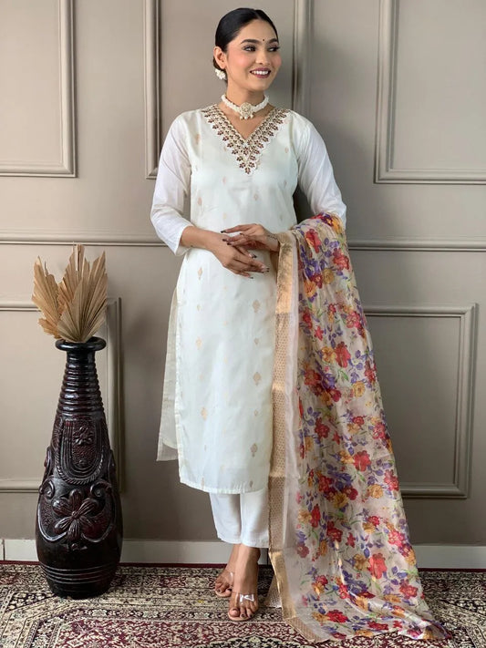 Woman in a white traditional outfit with a floral dupatta standing against a neutral wall.