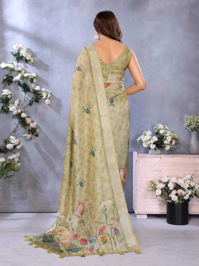 Woman wearing a light green saree with floral patterns in an indoor setting with flowers and a gray wall.