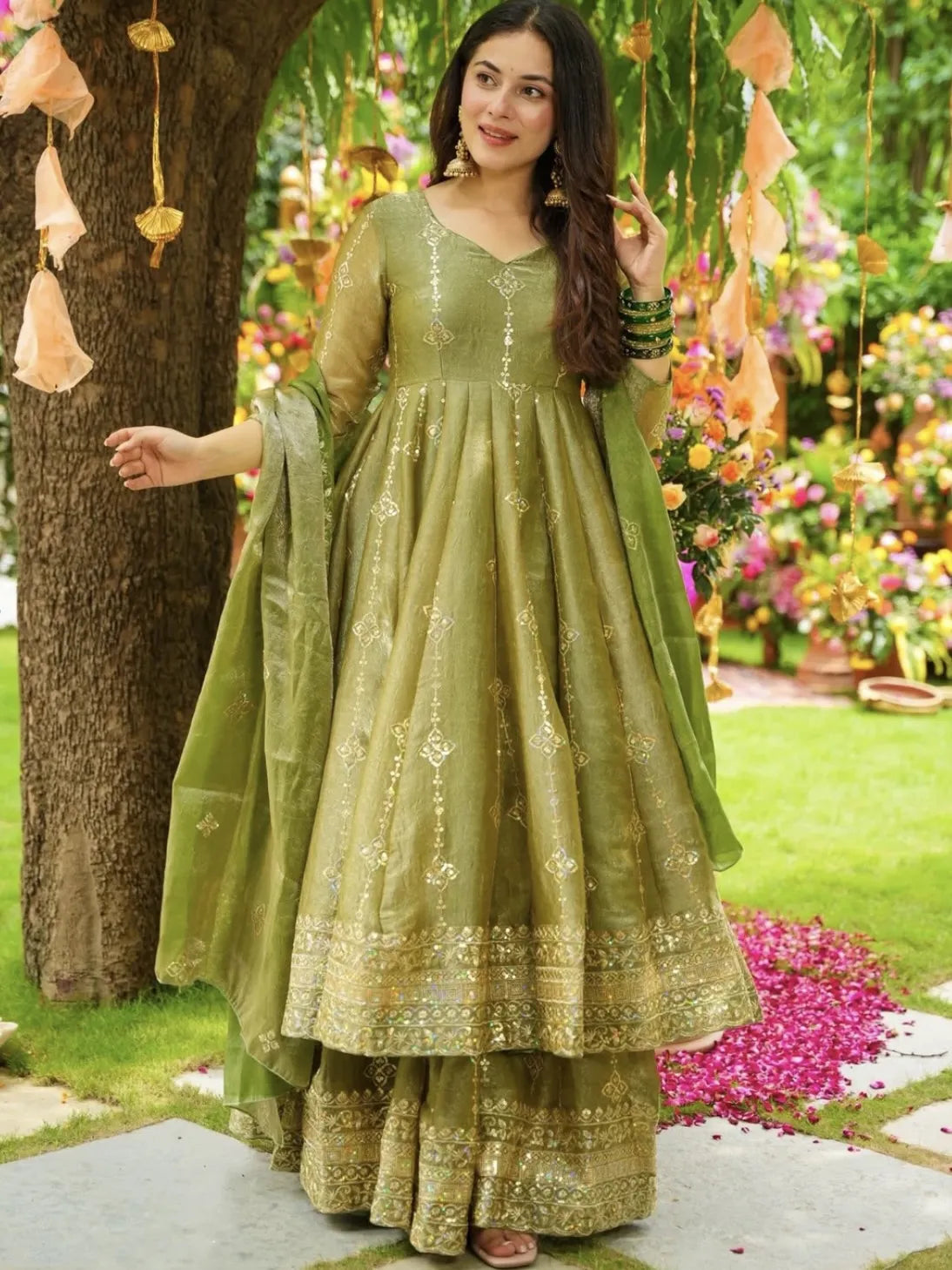 Woman in a green traditional outfit standing outdoors with floral decorations.