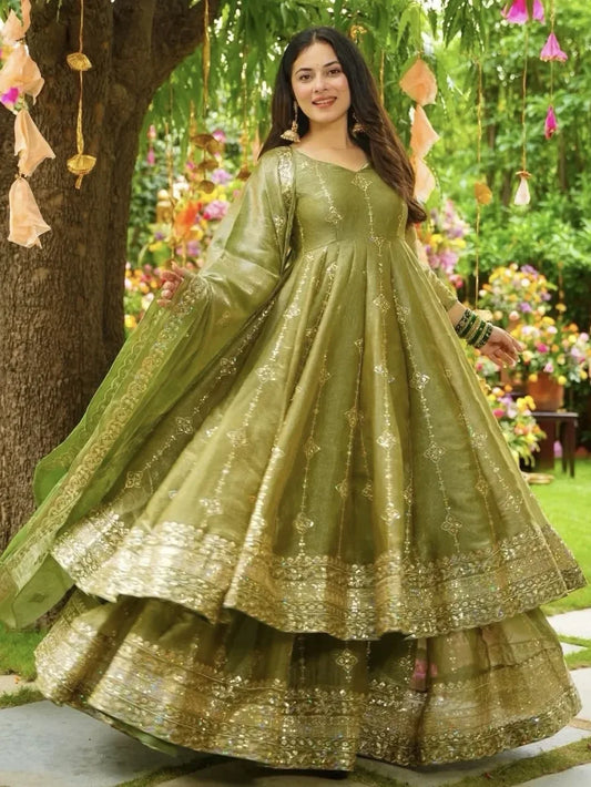 Woman in a green traditional outfit standing outdoors with floral decorations.