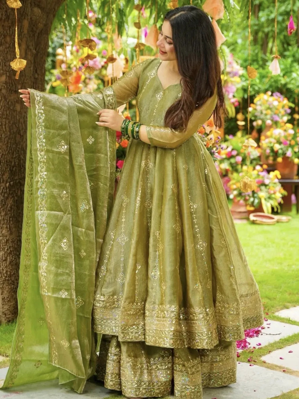 Woman in a green traditional outfit holding a dupatta in a garden setting