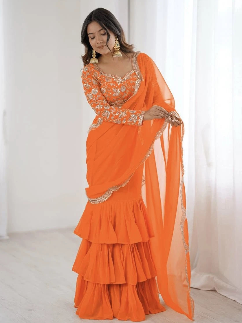 Woman wearing an orange saree with intricate designs in a minimalistic setting