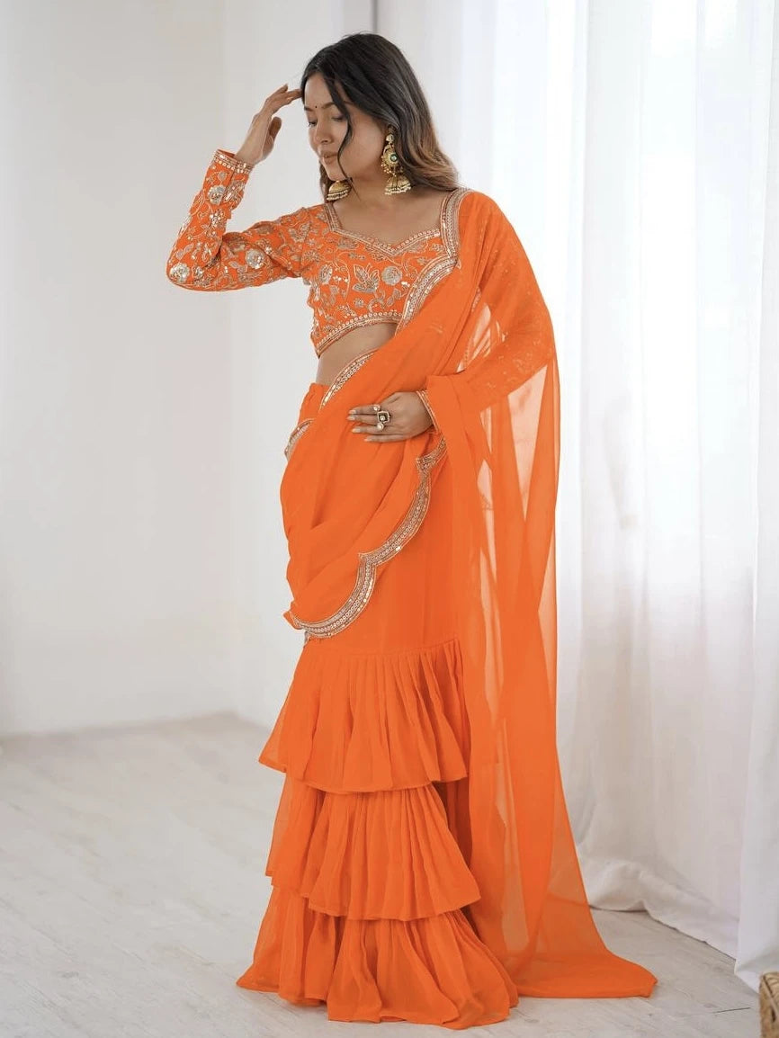 Woman wearing an orange saree with gold embroidery against a white background