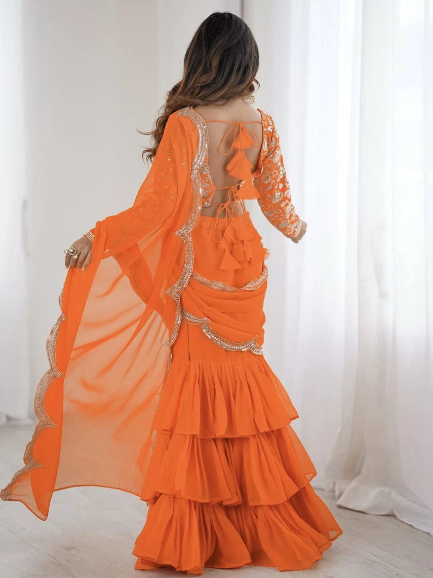 Orange saree with gold detailing worn by a person, against a white curtain background