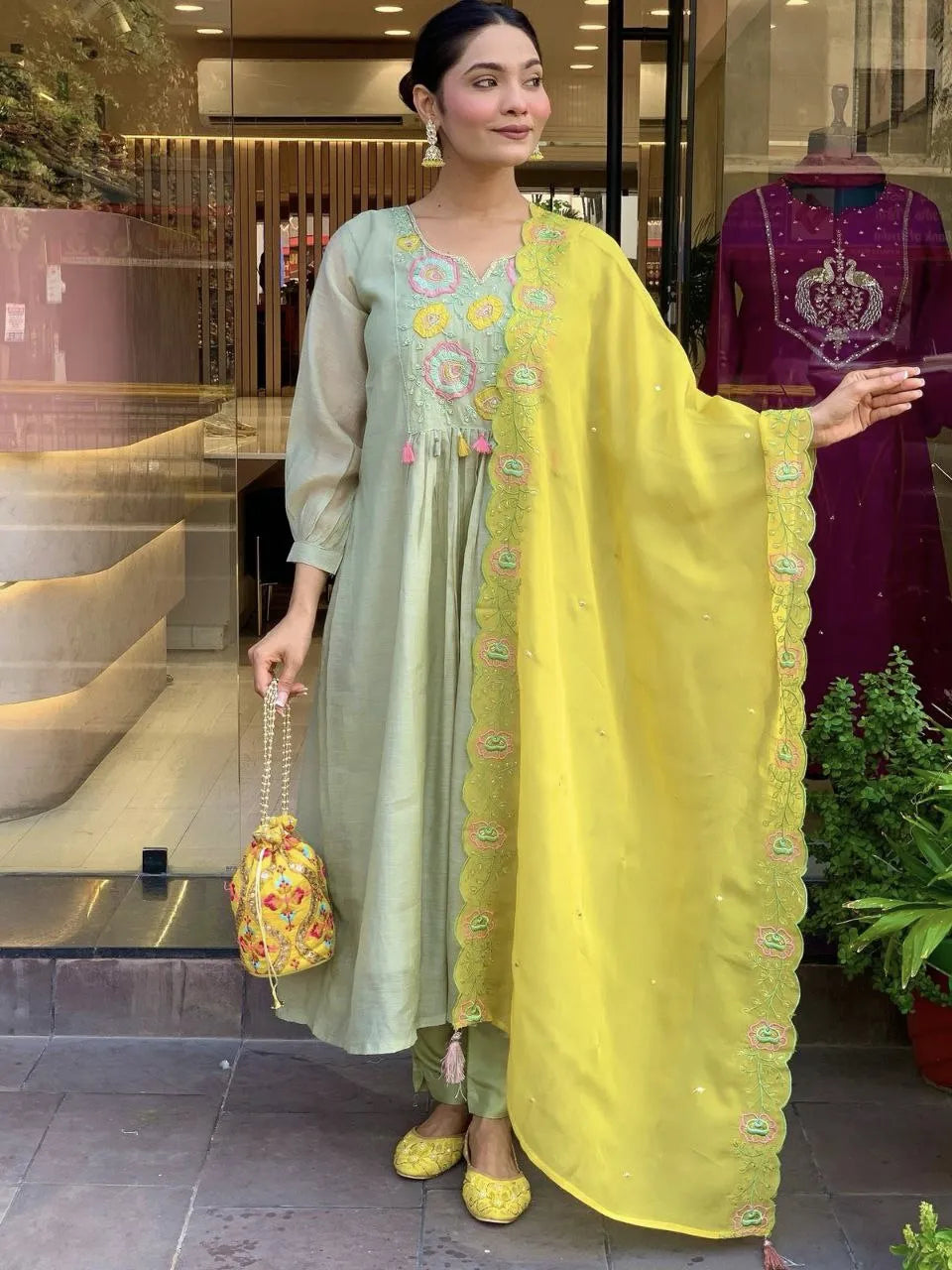 Woman in a light green embroidered outfit with a yellow dupatta in an indoor setting