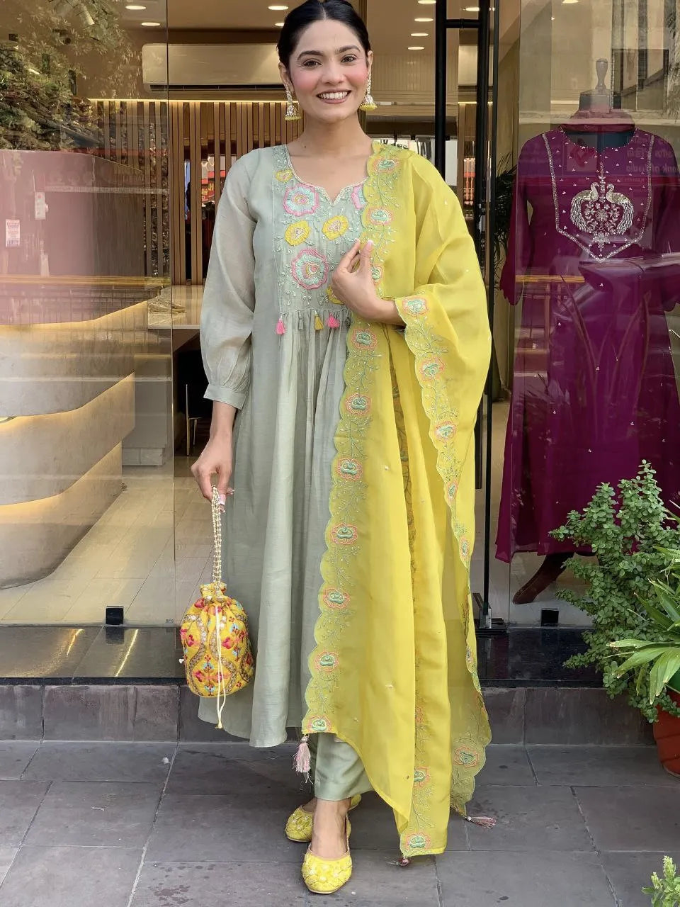 Woman in a light gray and yellow traditional outfit standing in front of a store with mannequins.