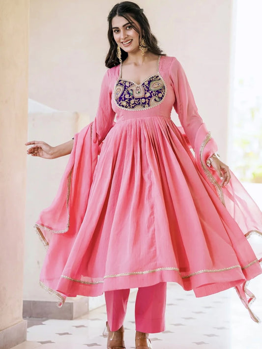Woman wearing a pink traditional outfit with intricate designs indoors.