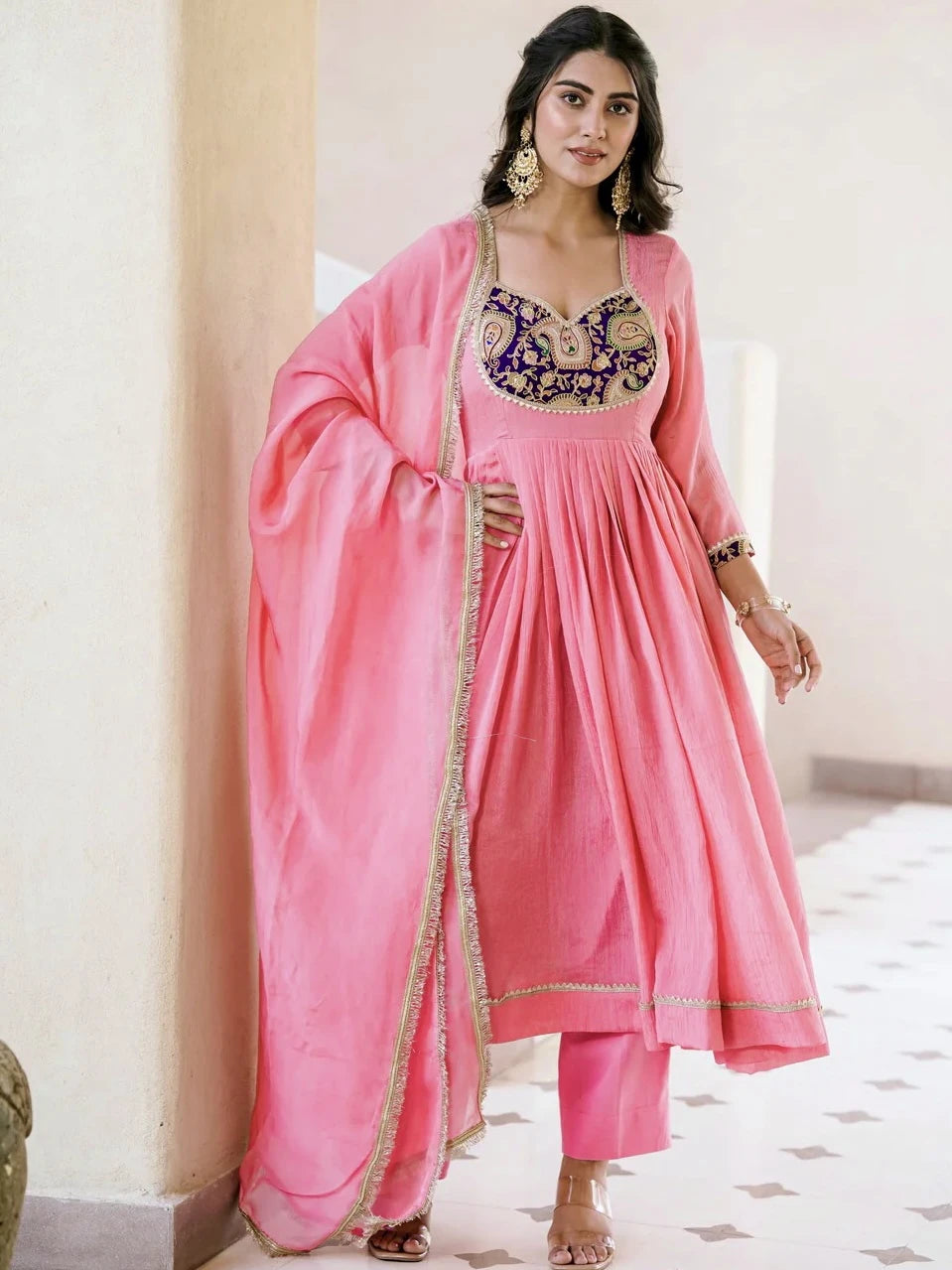 Woman wearing a pink traditional outfit with intricate designs indoors.