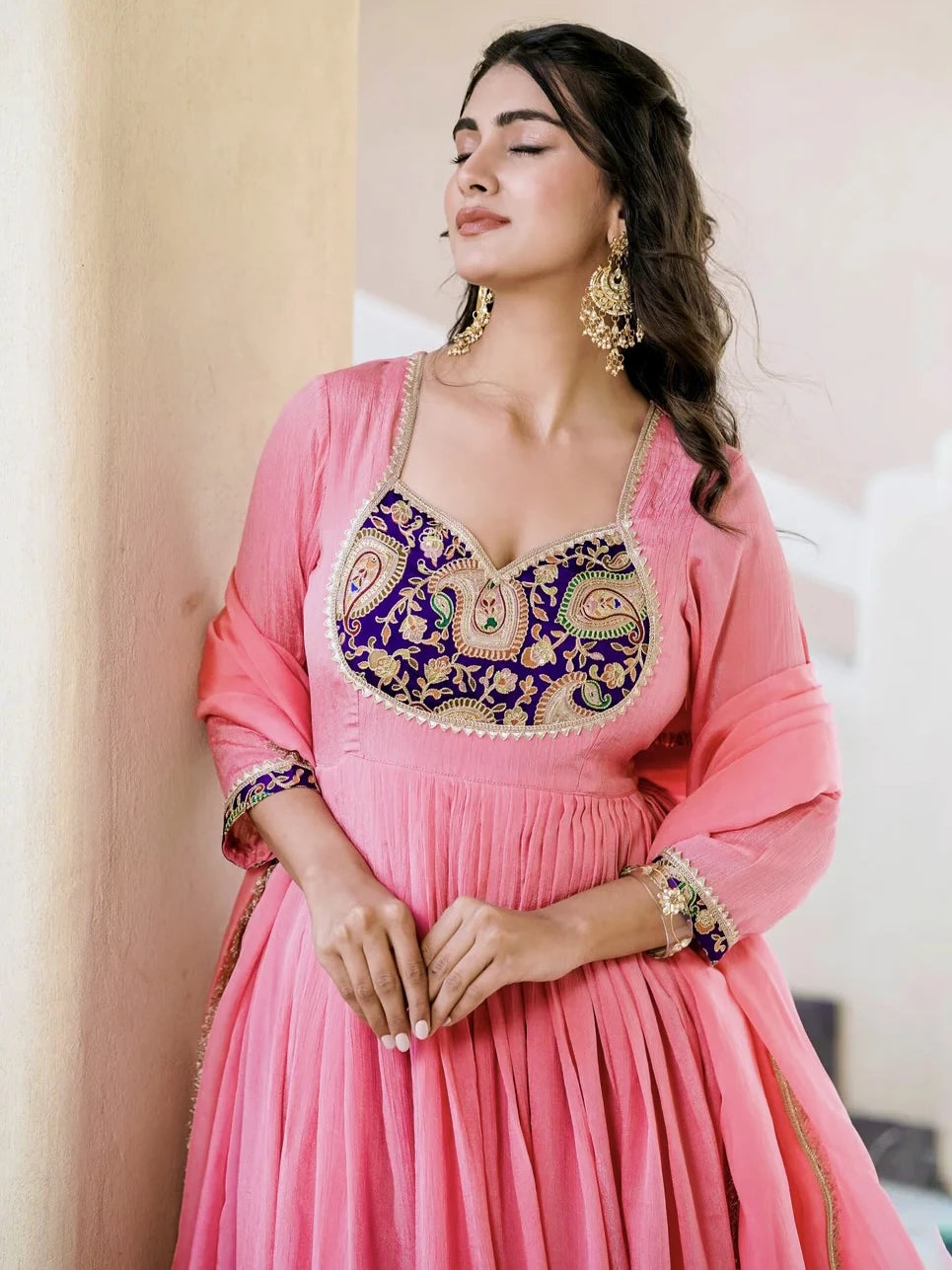 Woman wearing a pink traditional outfit with intricate blue and gold embroidery.