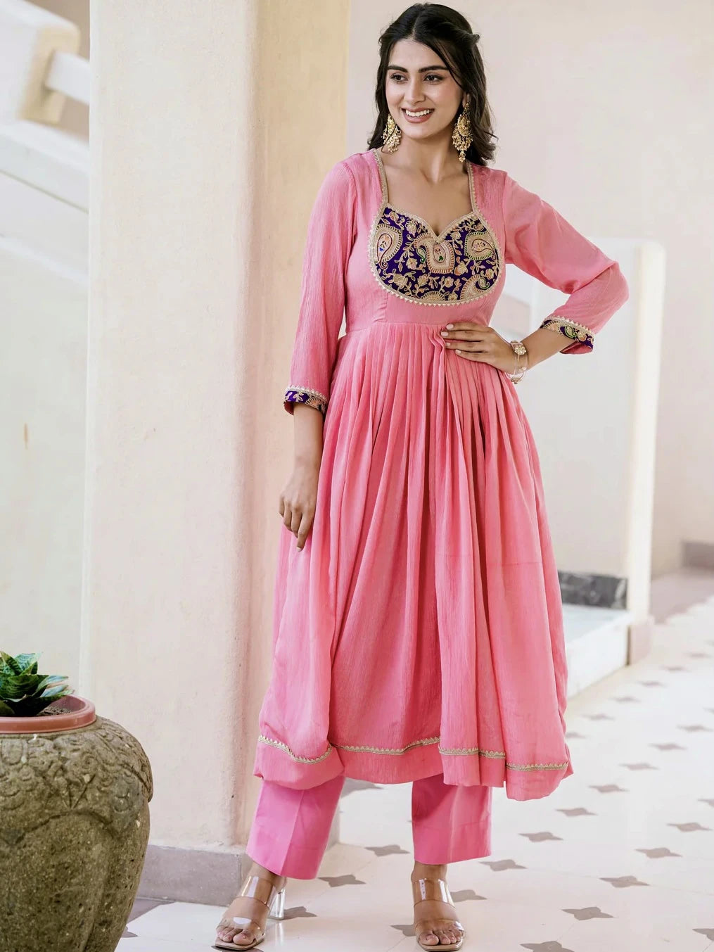 Woman wearing a pink traditional outfit with intricate embroidery in a bright room.