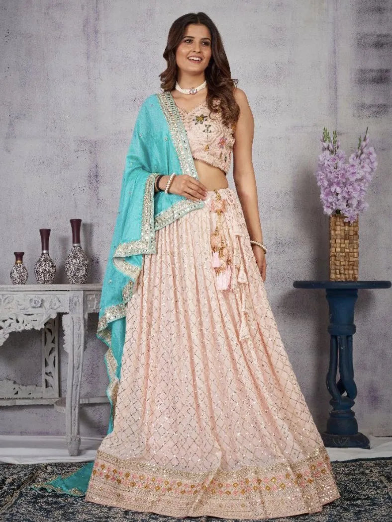 Woman in a traditional outfit with a light blue dupatta and pink lehenga, standing against a gray textured wall.