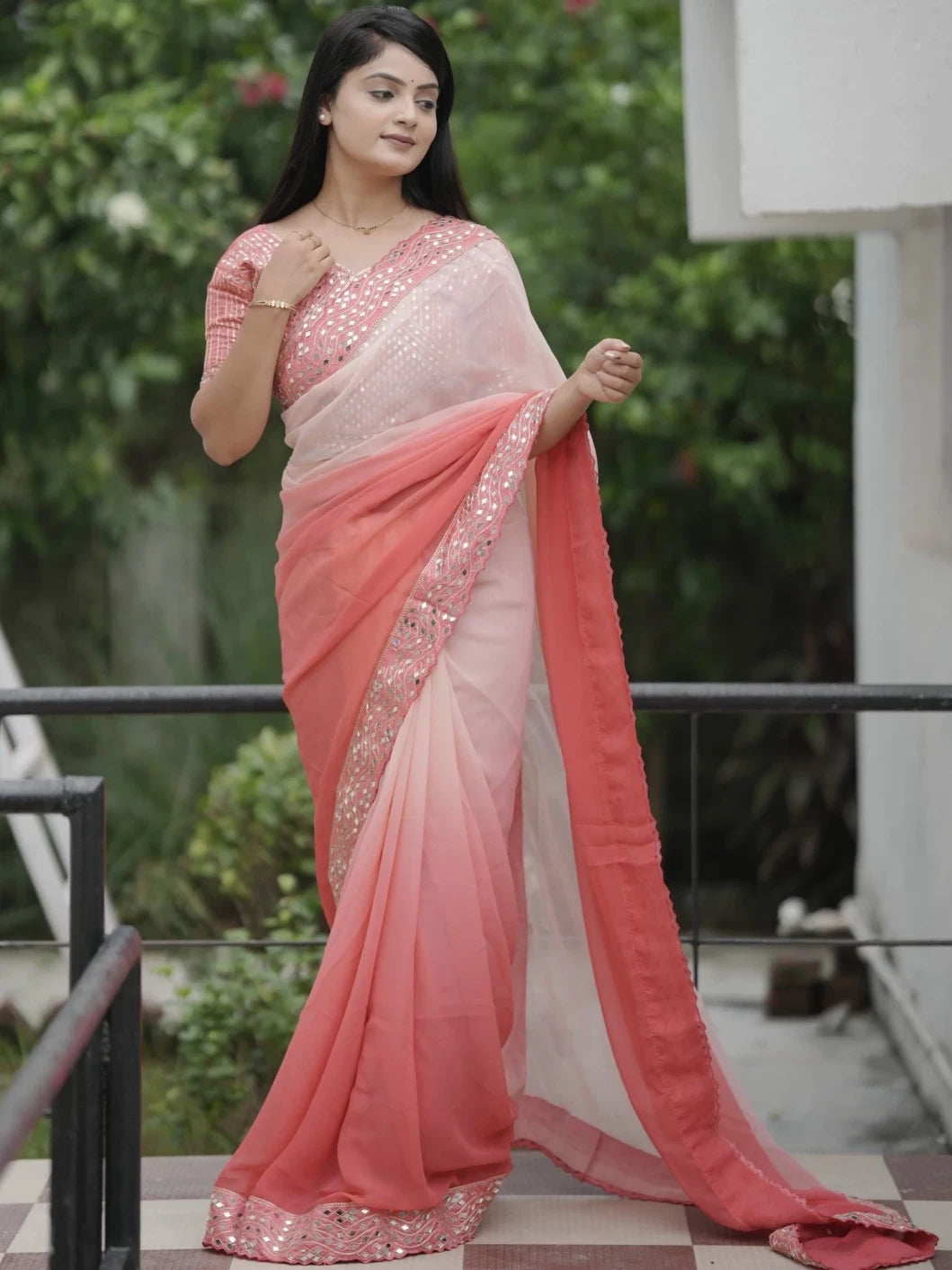Woman wearing a pink and white saree with a blurred green background