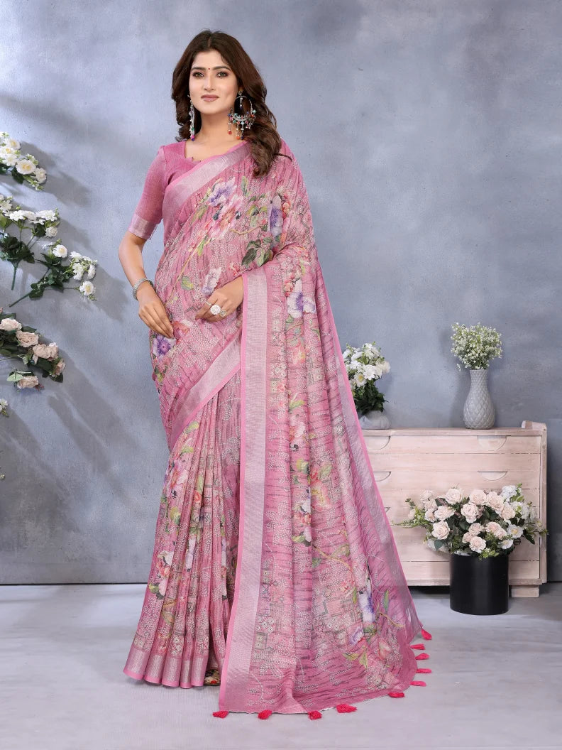 Woman wearing a pink saree with floral patterns in a decorative setting with flowers and a gray background.