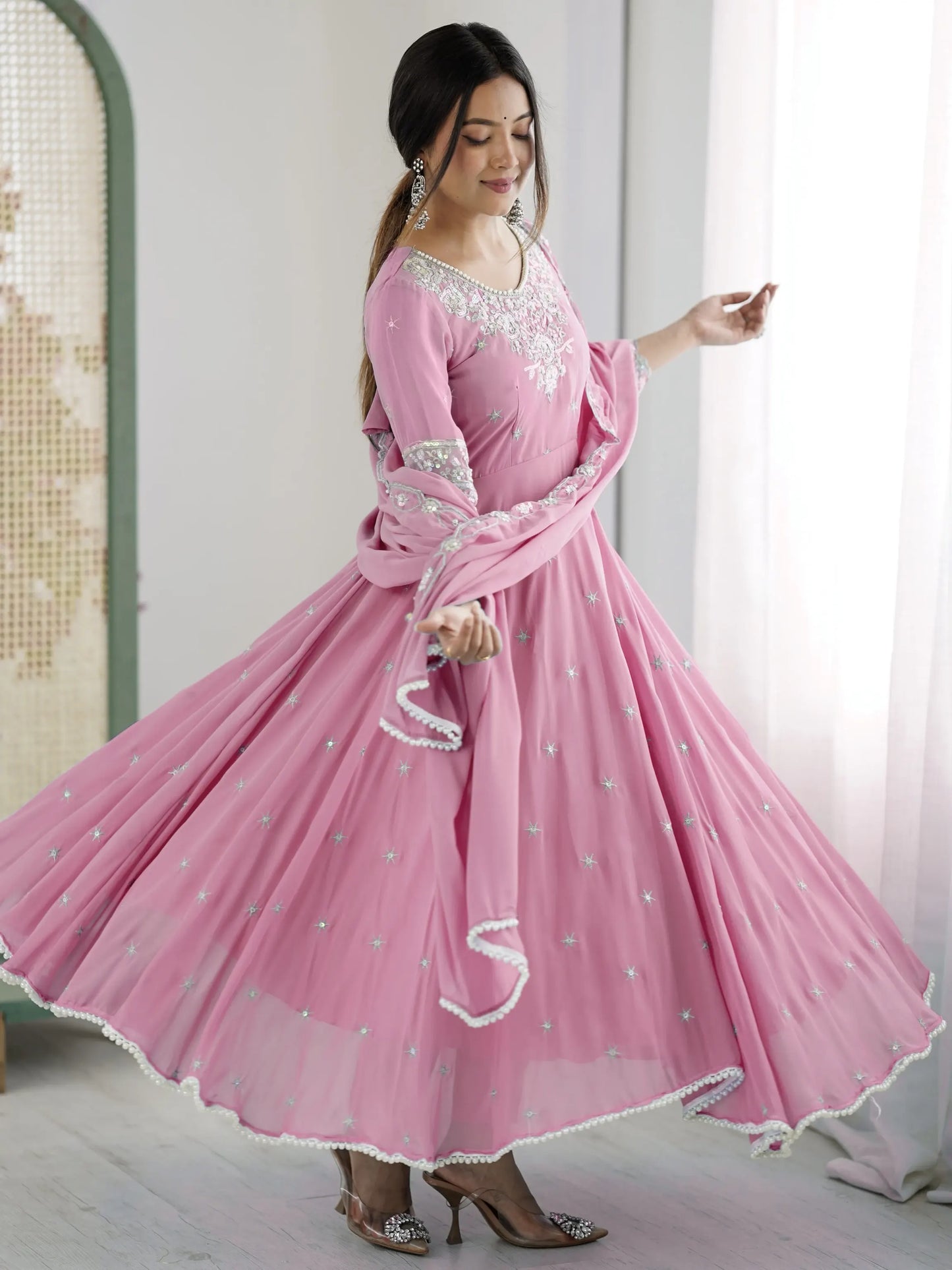 Woman wearing a pink traditional outfit with white embroidery in a bright room.