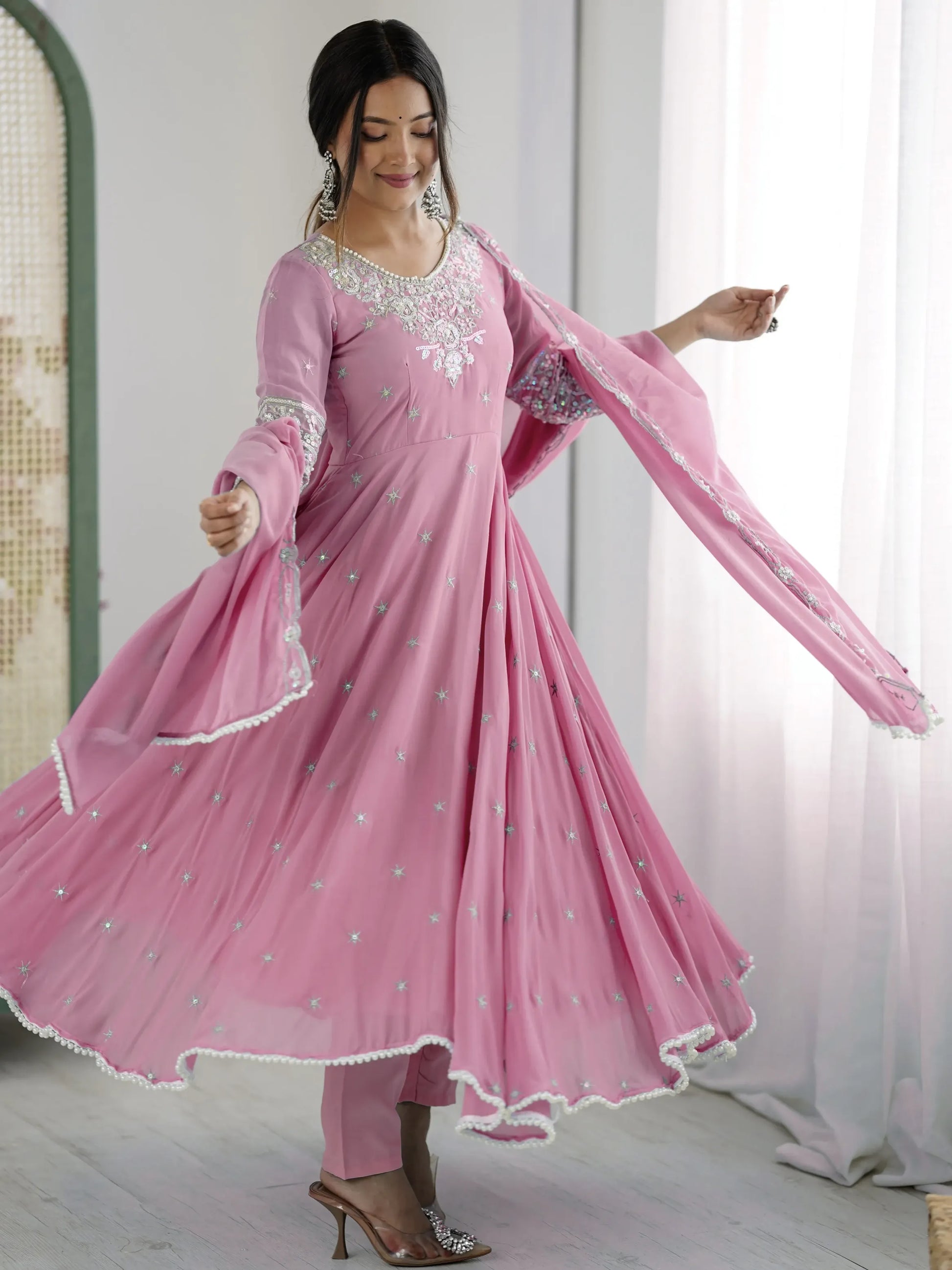 Woman wearing a pink traditional outfit with white embroidery in a bright room.