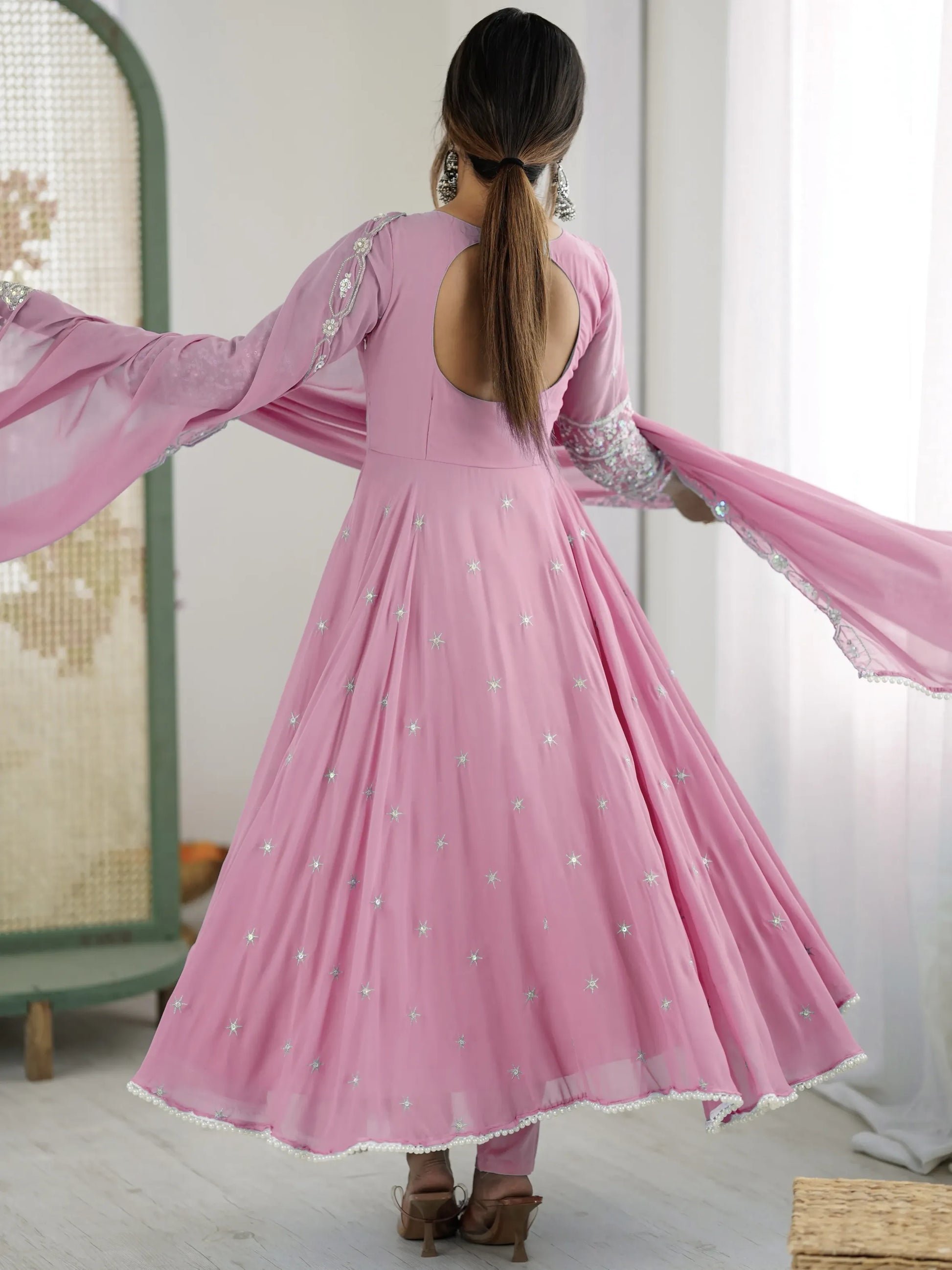 Woman wearing a pink dress with long sleeves and open back, standing indoors.