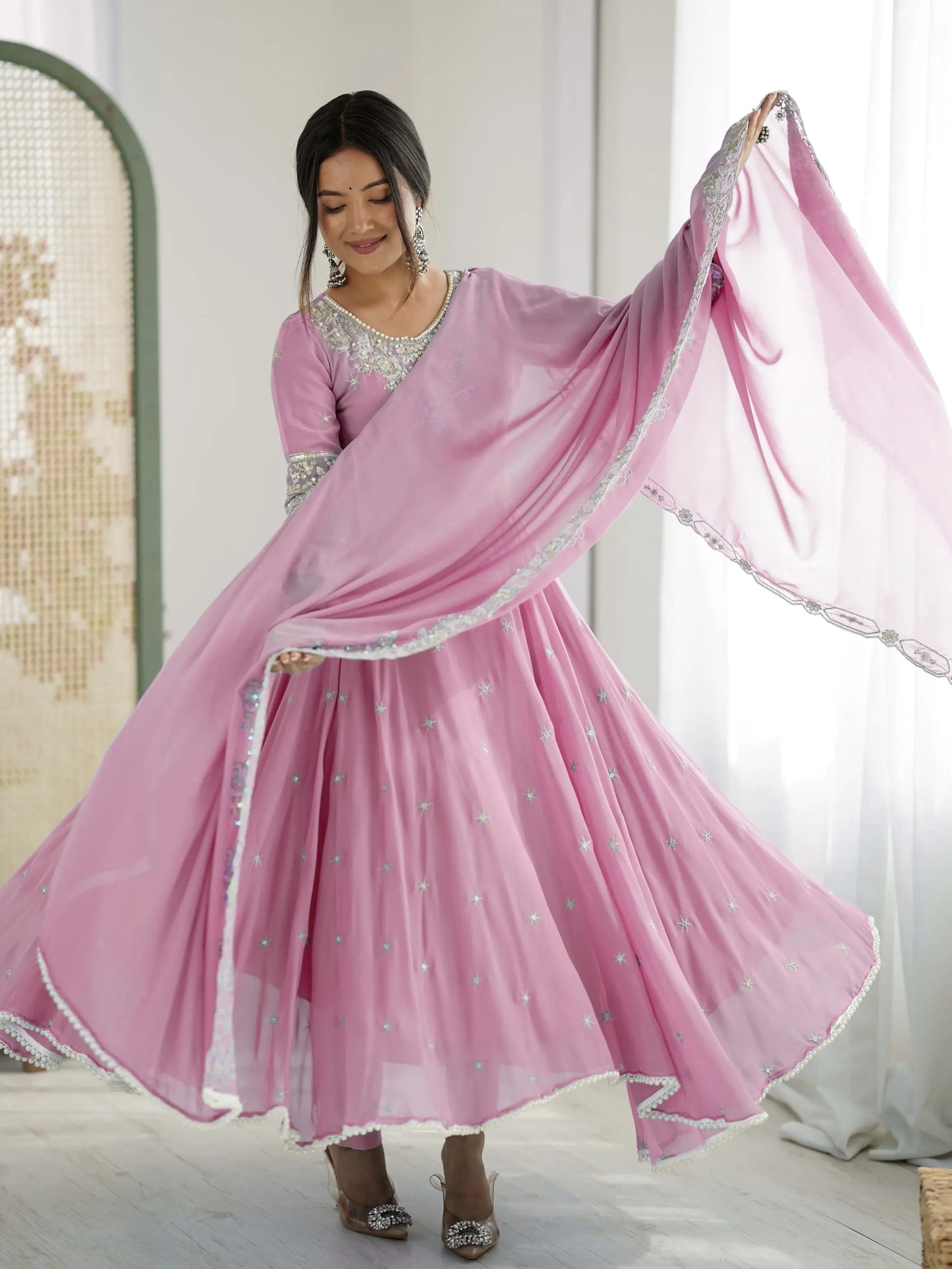 Woman in a pink traditional outfit with a matching dupatta, standing indoors.