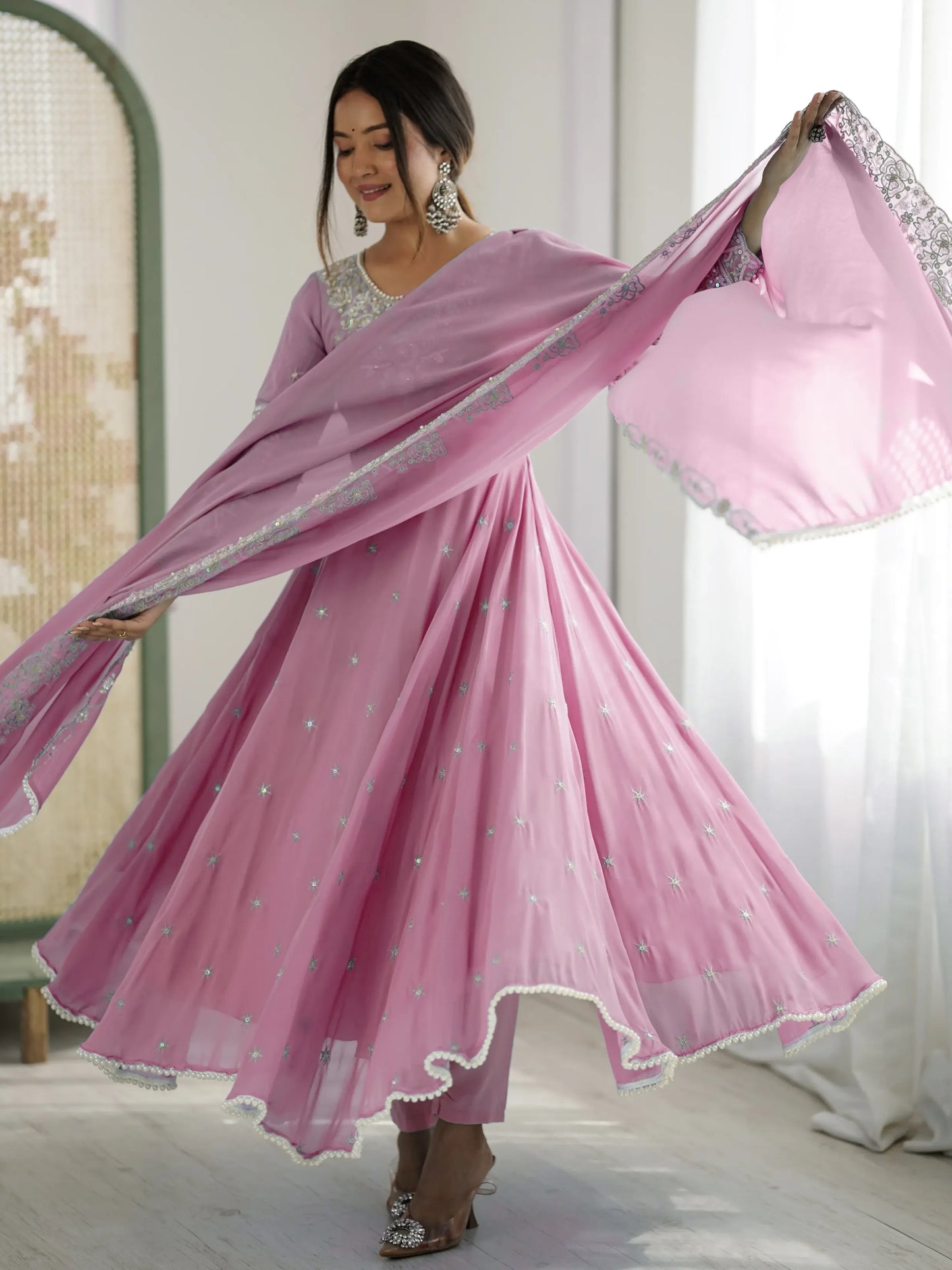Woman in a pink traditional outfit with a matching dupatta, standing indoors.