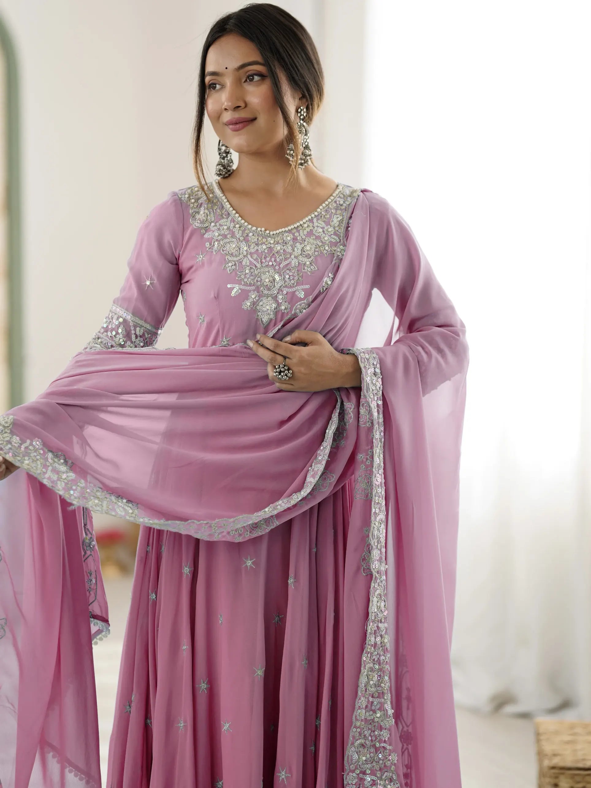 Woman wearing a pink saree with silver embroidery in a neutral setting
