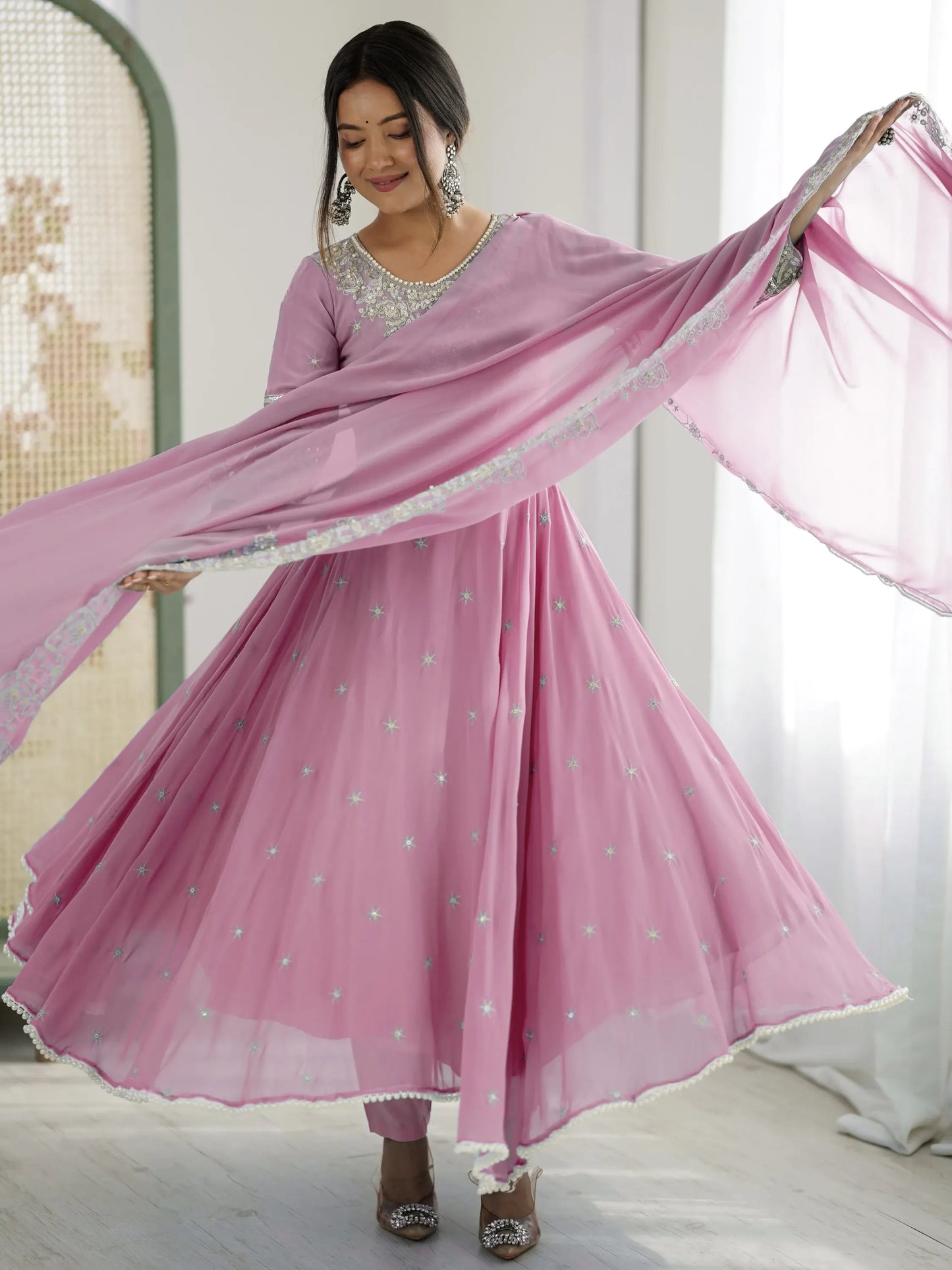 Woman in a pink traditional outfit with a matching dupatta, standing indoors.