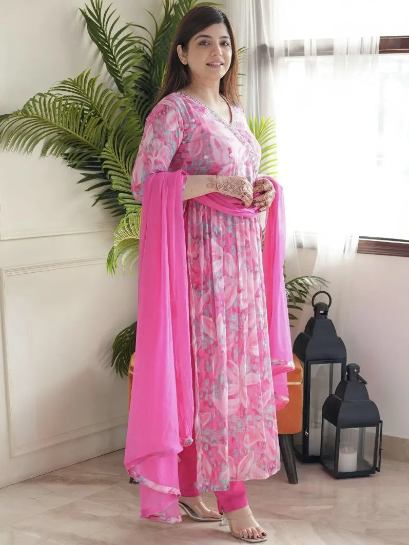 Woman in a pink and white floral outfit with a pink dupatta standing indoors.
