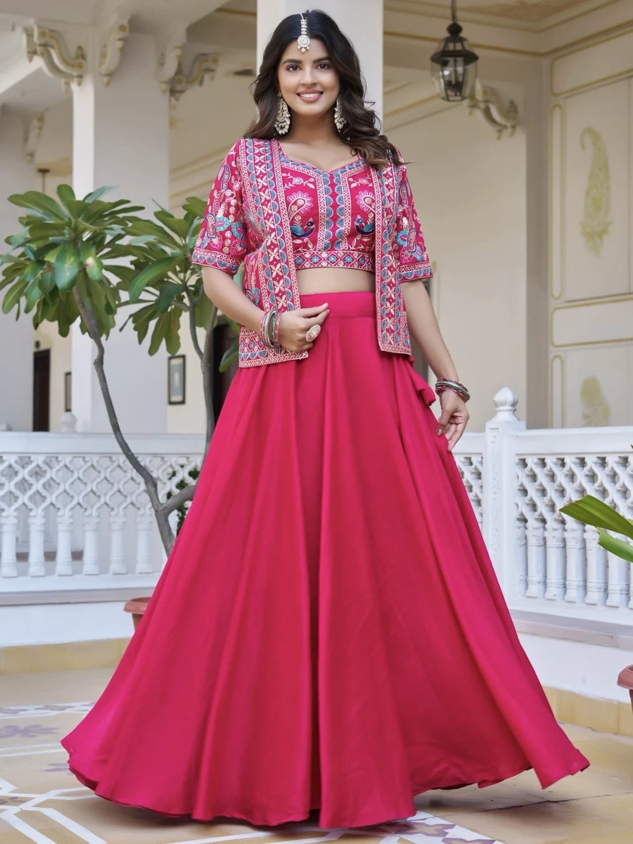 Woman in a pink traditional outfit with intricate patterns in an elegant indoor setting.