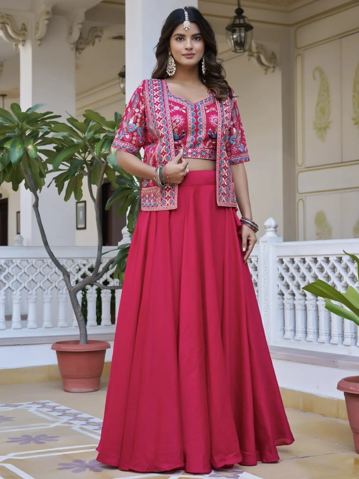 Woman in a pink traditional outfit standing in an outdoor setting with decorative elements.