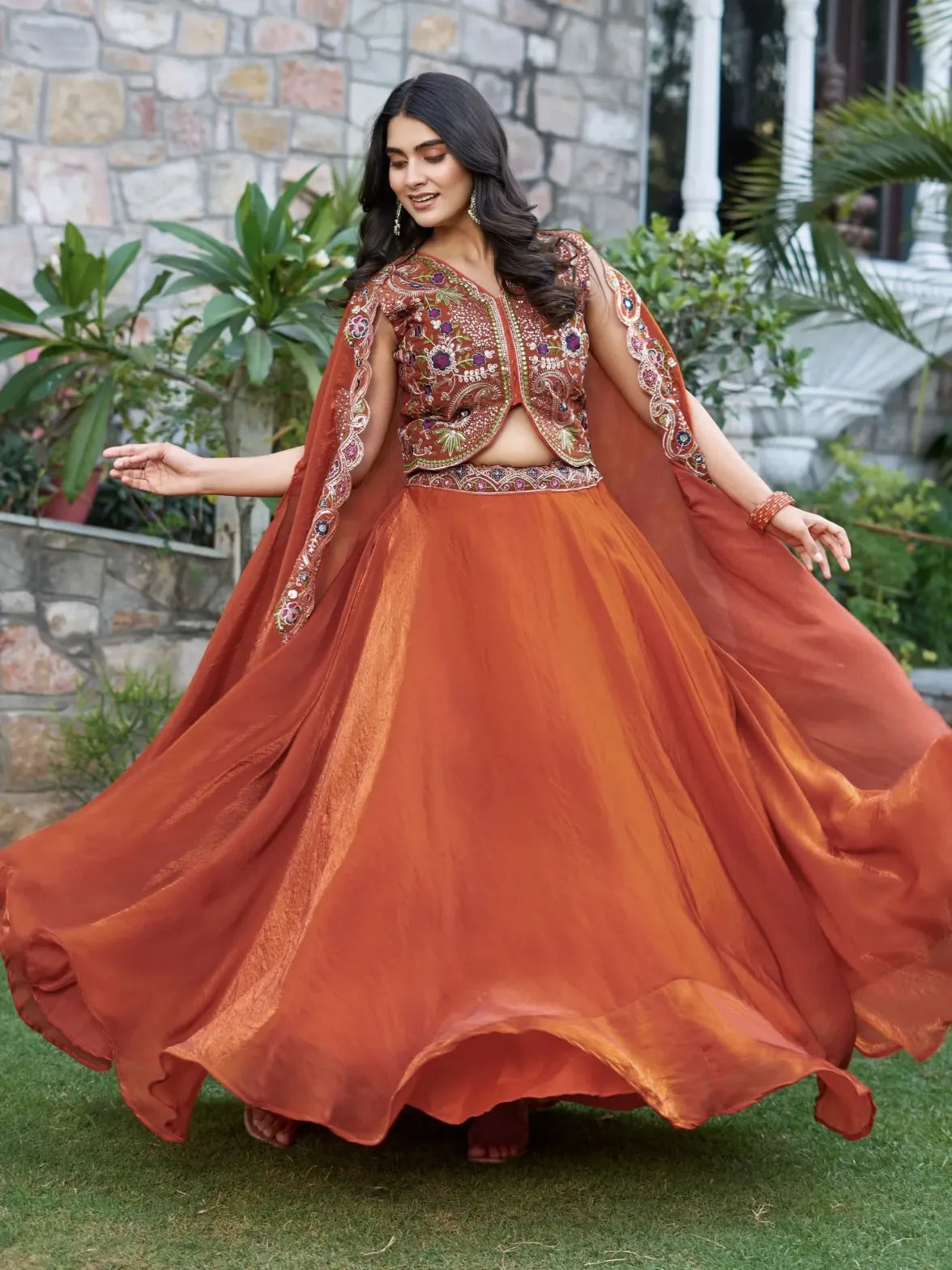 Woman in a traditional orange outfit with intricate designs, standing outdoors.