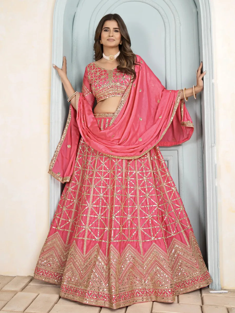 Woman wearing a pink embroidered lehenga with a matching dupatta, standing in a doorway.