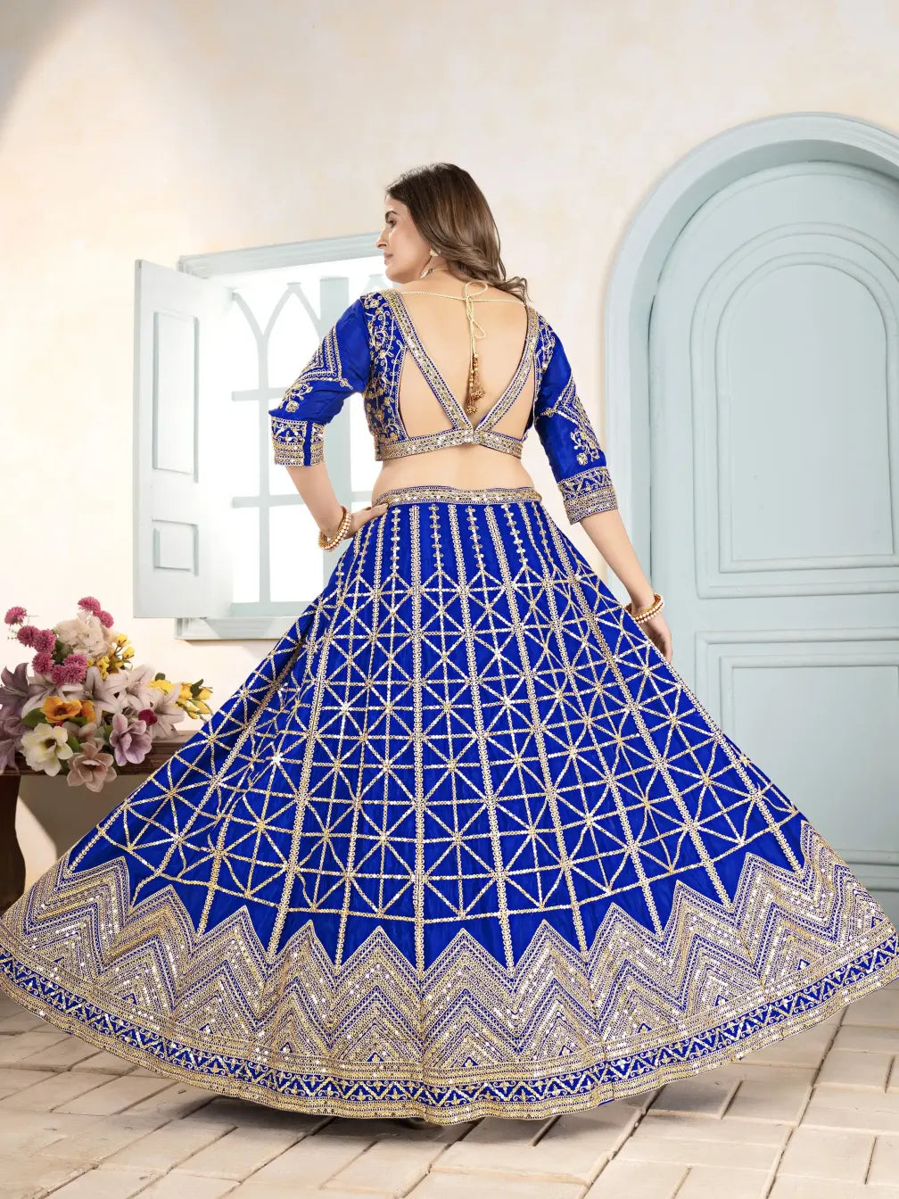 Woman wearing a blue and white embroidered traditional outfit with a white door and flowers in the background