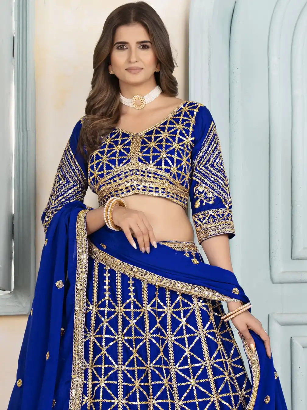 Woman wearing a blue embroidered traditional outfit with gold detailing.